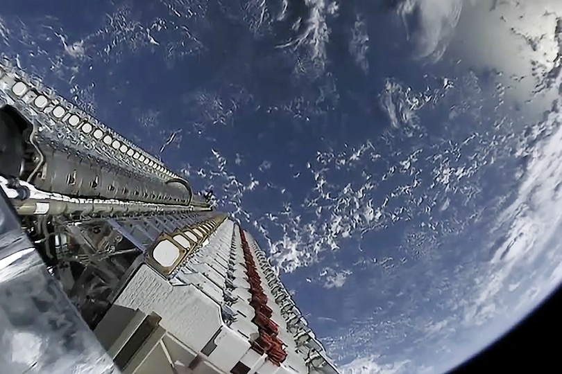 A camera on board a satellite looks down towards Earth showing part of the satellite and the planet.