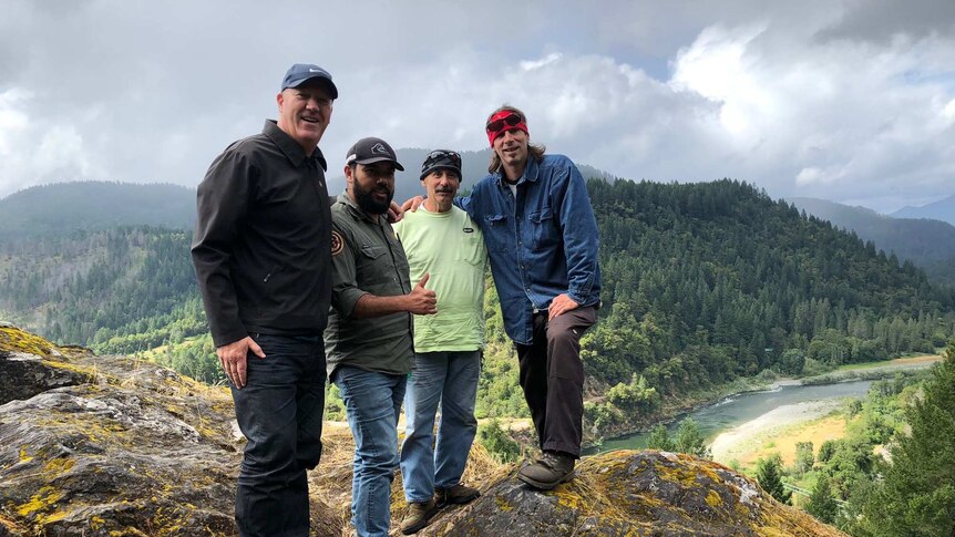 Scott Falconer stands with three men on top of a hill over looking a river and forest on a cloudy day