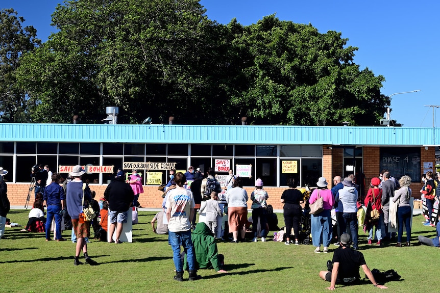 A crowd of people surround a building holding signs and listening to a person speaking