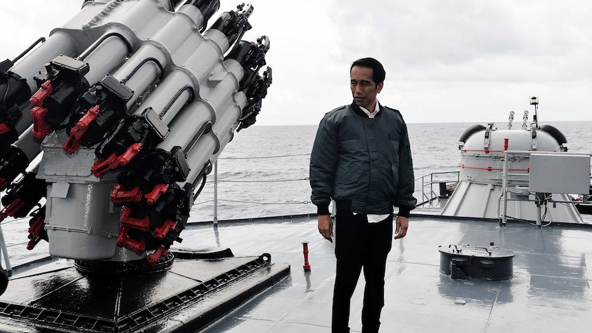 Indonesian President Joko Widodo looks at a weapon on board a warship.