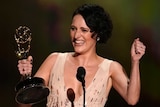 Phoebe Waller-Bridge smiles with an Emmy award, standing in front of a microphone on stage