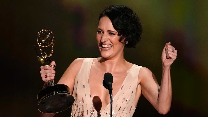 Phoebe Waller-Bridge smiles with an Emmy award, standing in front of a microphone on stage