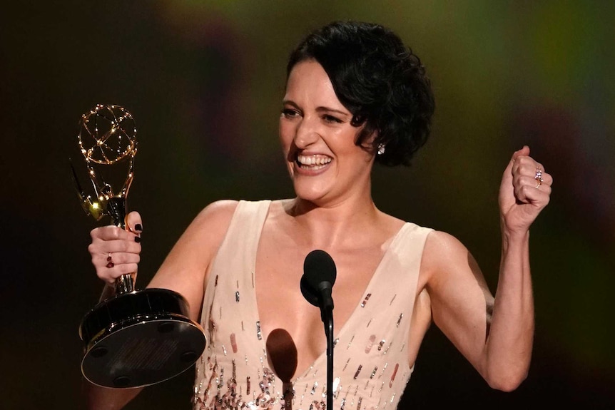 Phoebe Waller-Bridge smiles with an Emmy award, standing in front of a microphone on stage