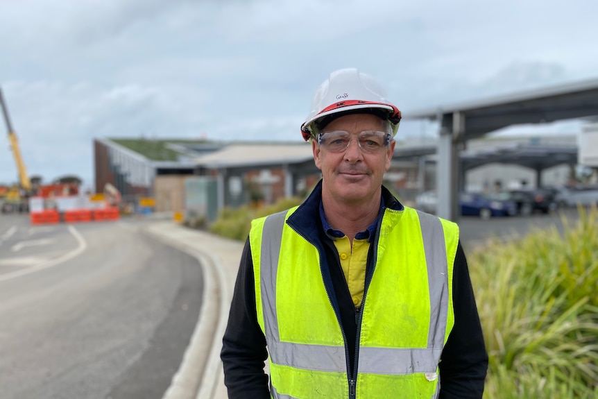 A middle-aged man wearing a high vis vest and protective goggles standing near a building site
