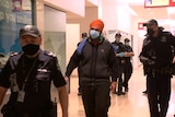 A man wearing an orange turban and a face mask is surrounded by police in an arcade