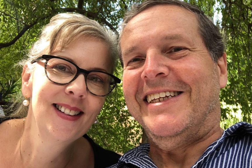 Selfie headshot of a smiling middle aged couple with trees in the background
