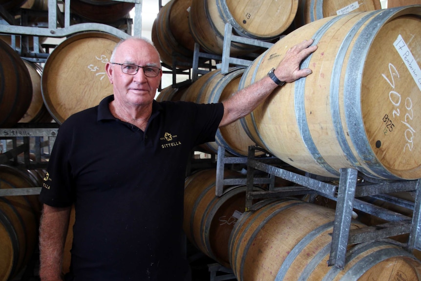 Ron Page stands alongside barrels of wine, with his hand on one of them.