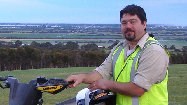 Colin Lawson wearing high vis leaning on quad bike with field in the background