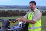 Colin Lawson wearing high vis leaning on quad bike with field in the background