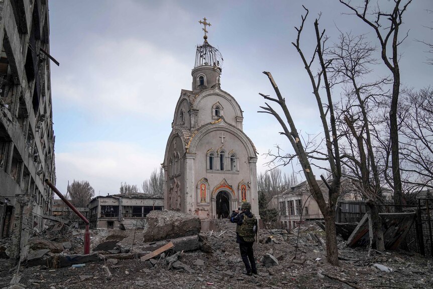 A Ukrainian serviceman takes a photograph of a damaged church after shelling.