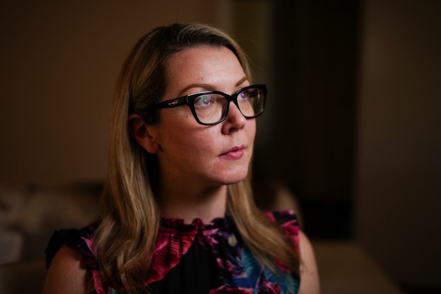 A young white woman with long light brown hair and glasses looking off-camera.