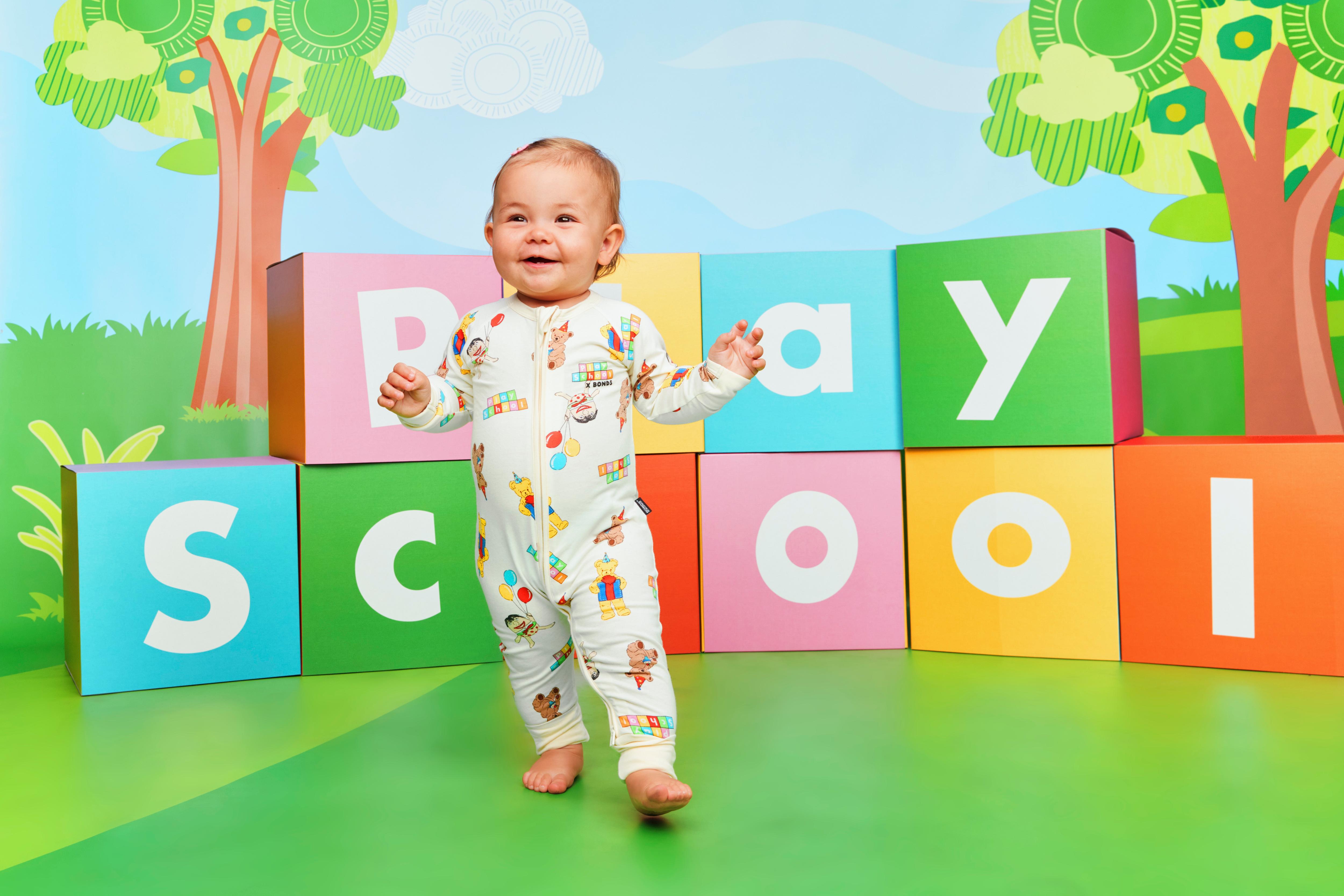 Baby wearing Play School outfit in front of colourful blocks