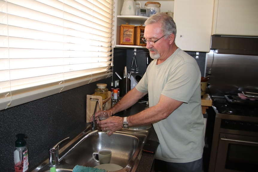 A man standing at his kitchen sink, getting himself a glass of ater.