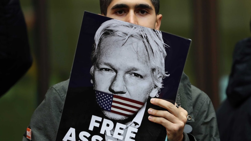 A portrait of a an Assange support with his face half covered by a "Free Assange" placard