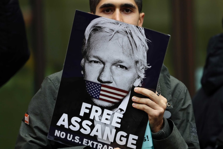 A portrait of a an Assange support with his face half covered by a "Free Assange" placard