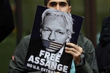 A portrait of a an Assange support with his face half covered by a "Free Assange" placard