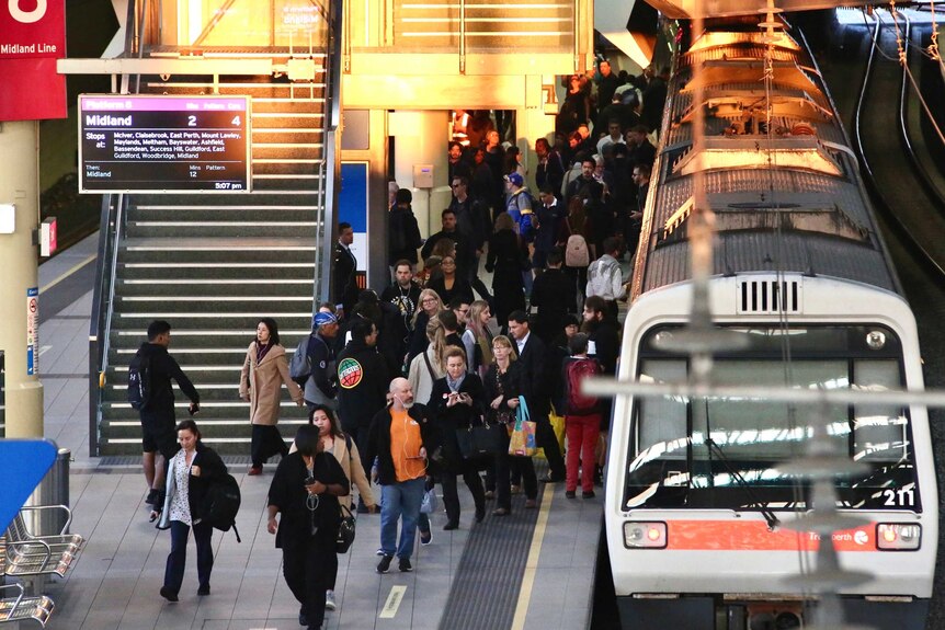 People crowd a platform at Perth station in the late afternoon light.