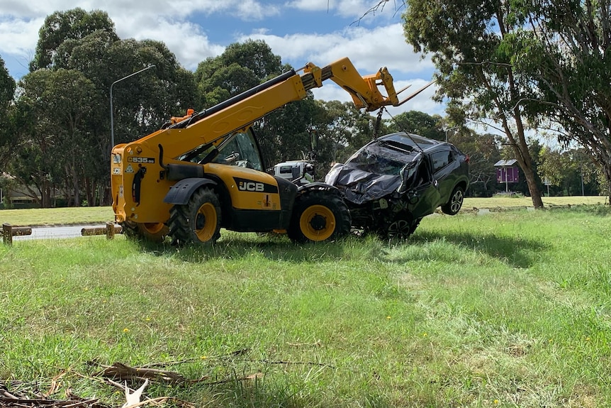 A yellow crane lifts a dark coloured car off the ground.