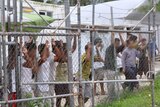 Asylum-seekers look through a fence at a detention centre