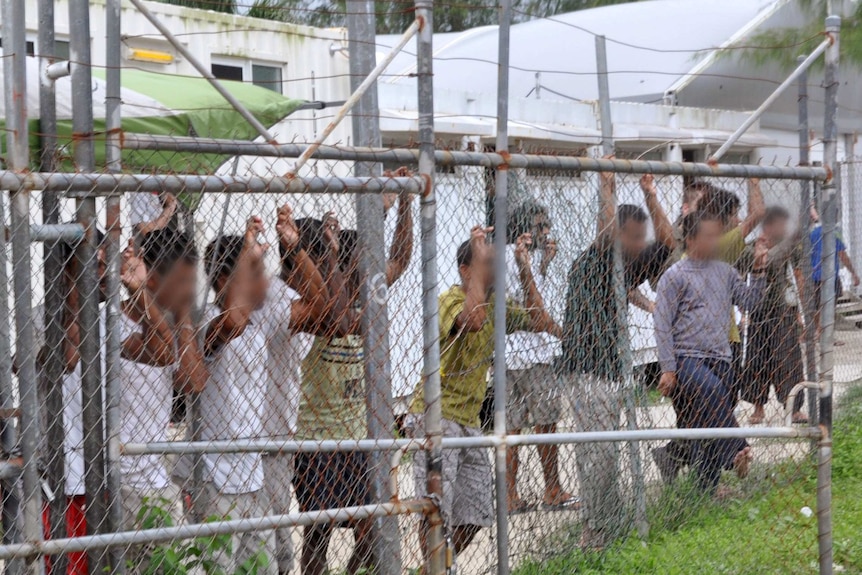 Asylum-seekers look through a fence at the Manus Island detention centre