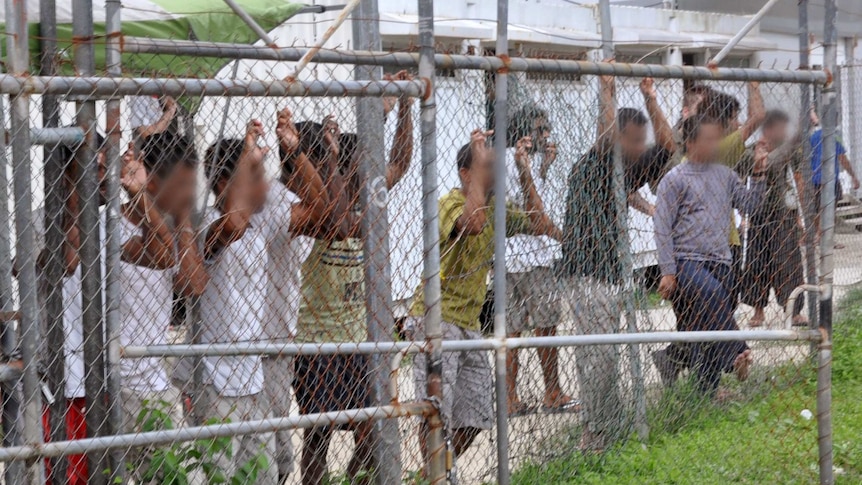 Asylum-seekers look through a fence at a detention centre