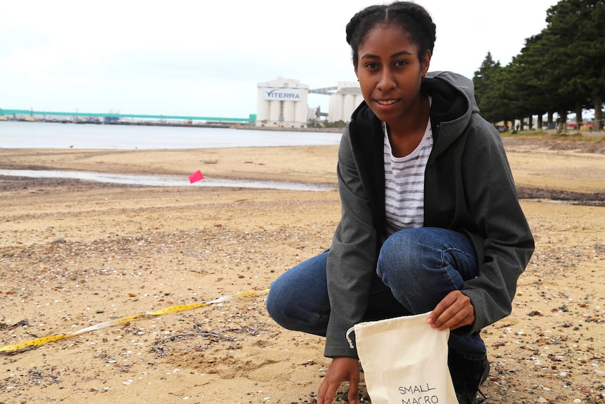 A young girl sits on a beach holding a bag labelled 'small macro'