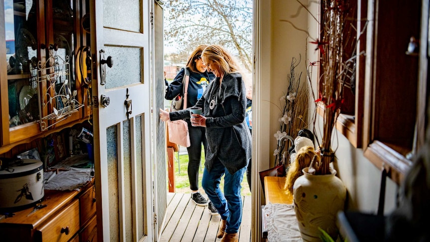 Donna walks into her home, seen through the doorway, with Sandy outside behind her.