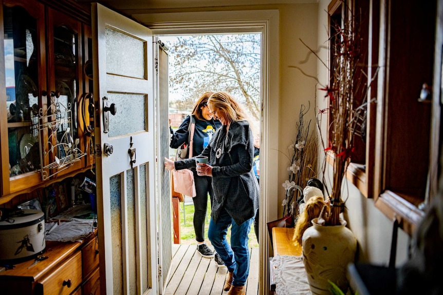 Donna walks into her home, seen through the doorway, with Sandy outside behind her.