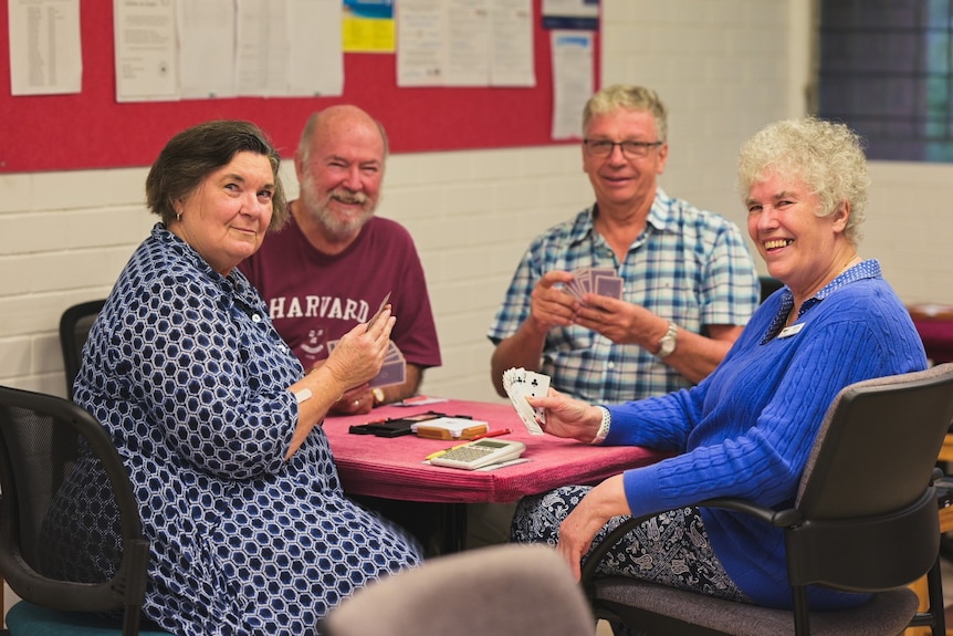 Four card players sit around a table.