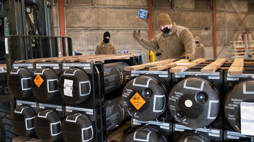 Men inspect piles of weapons and other equipment bound for Ukraine.