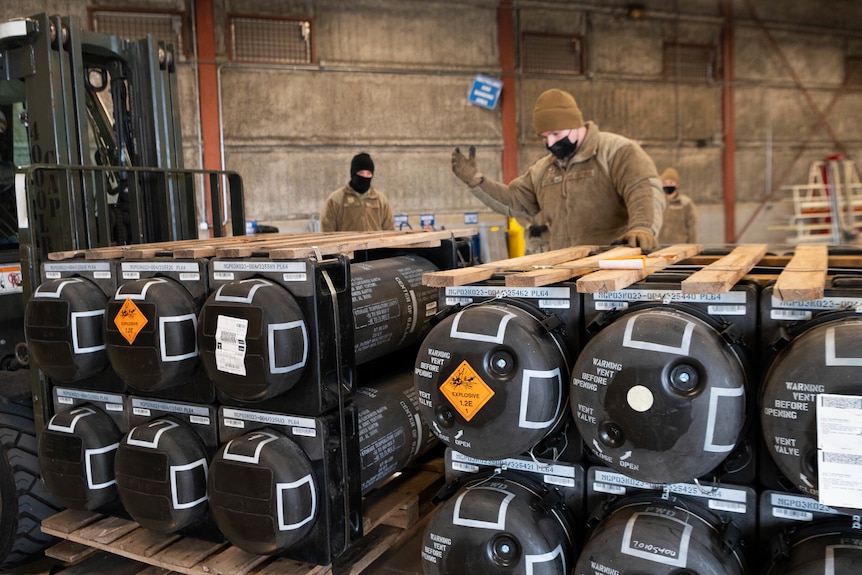 Men inspect piles of weapons and other equipment bound for Ukraine.