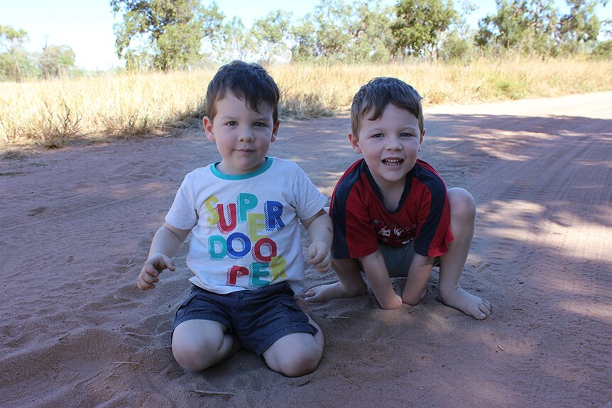 One-and-a-half year old Dustin and five-year-old Ned sit in the red dirt on their station.