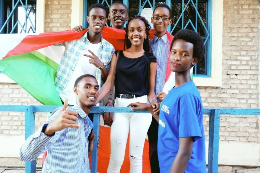 Two girls and four boys from the Burundi robotics team smile and pose with the Burundi flag.