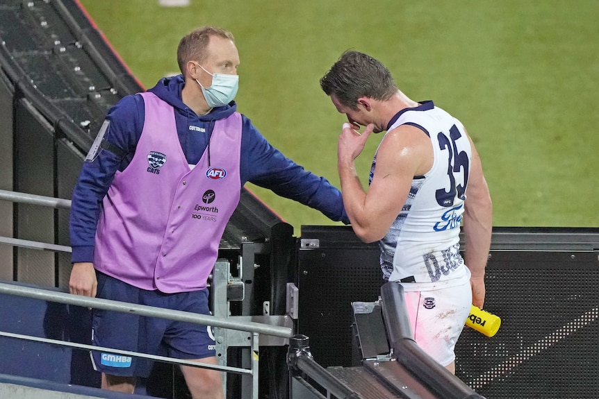 AFL player Patrick Dangerfield rubs his face as a team official opens a gate for him to walk to the rooms after being hit.