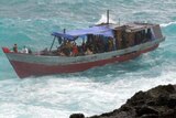 A boat carrying asylum seekers is bounced on rough surf before crashing into rocks off Christmas Island.