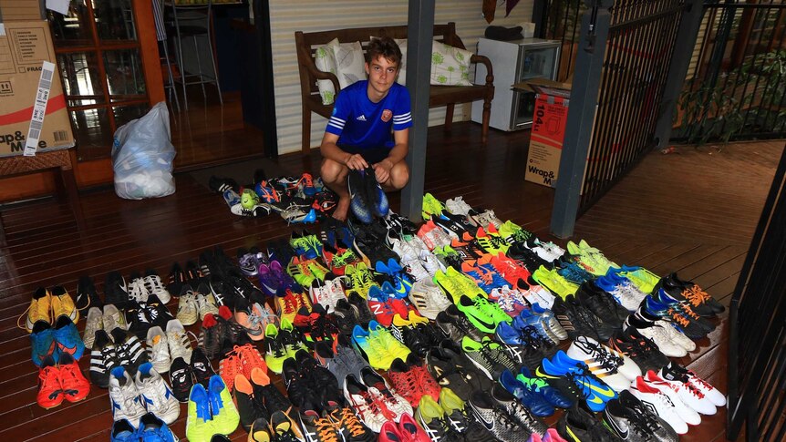 A boy sits surrounded by 200 multicoloured football boots