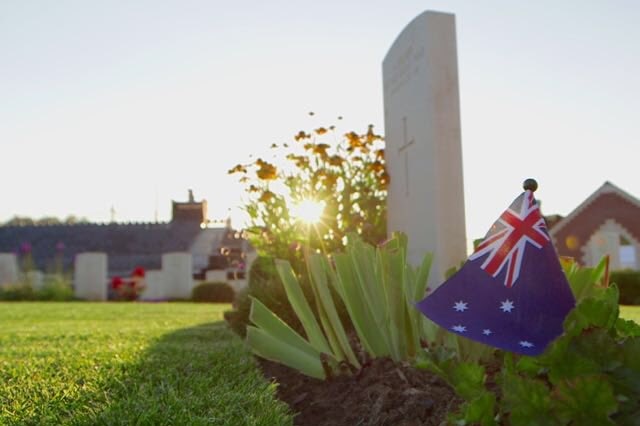 The sun rises behind a grave with an Australian flag in Fromelles.