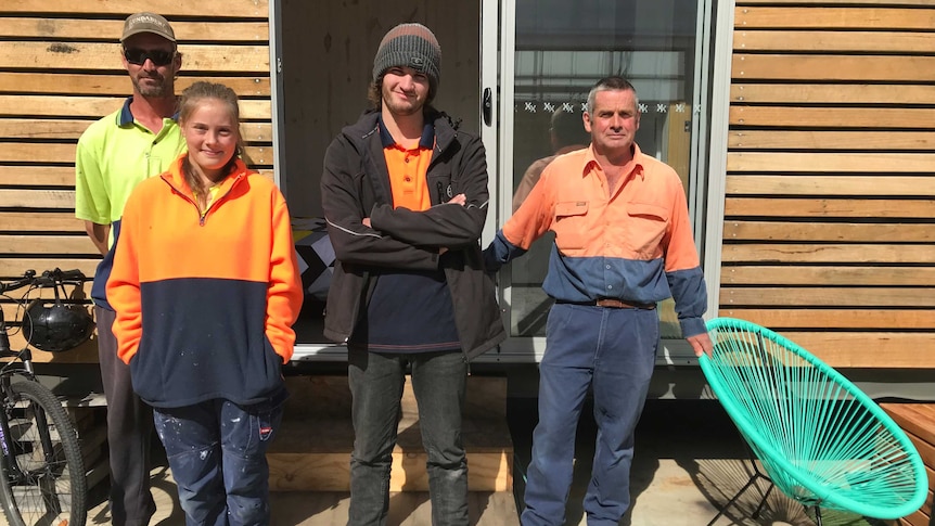 A team of volunteers stand outside a shipping container they converted to a tiny house.