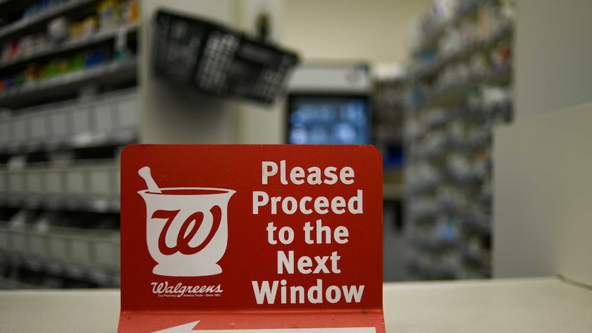 A sign directing customers to the next counter sits on the bench in a walgreens pharmacy