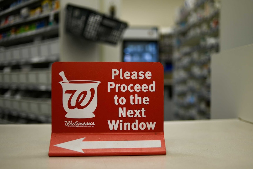 A sign directing customers to the next counter sits on the bench in a walgreens pharmacy