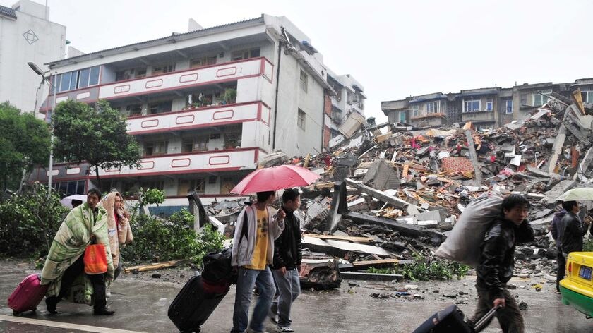 Residents carry their bags past a collapsed building