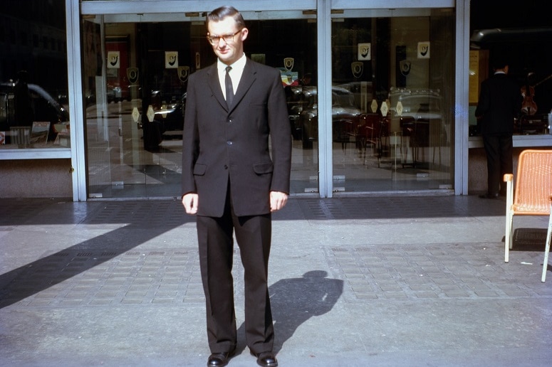Vincent Ryan pictured in Rome in 1966 wearing a black suit and glasses, standing outside an unspecified location.