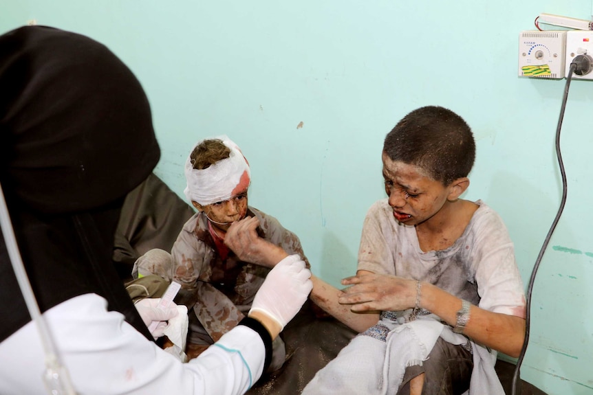 Two bloodied and bandaged boys are treated by a doctor.