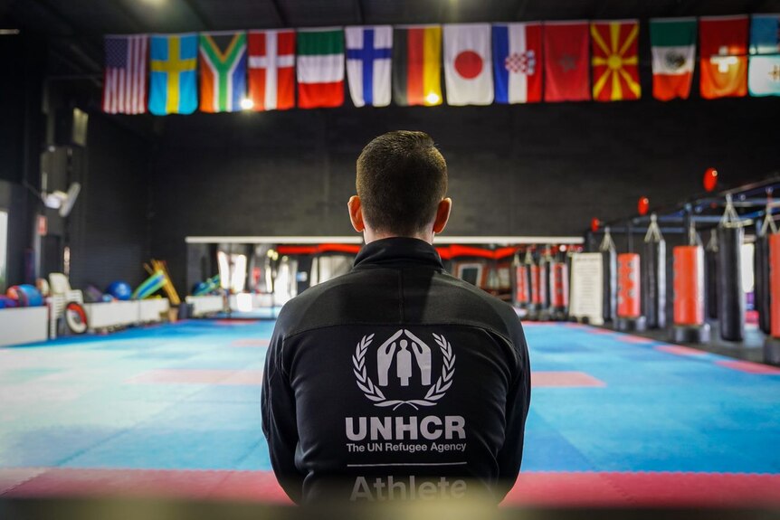 Asif Sultani wearing a black UNHCR tracksuit faces away from the camera, looking at world flags