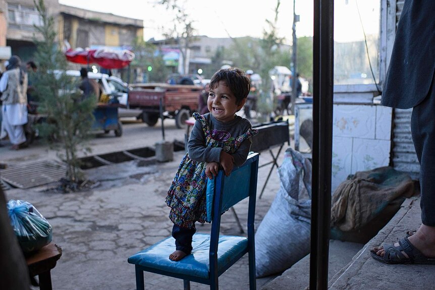 Shaesta, a three-year-old girl with one leg, smiles as she stands outside her fathers shop.