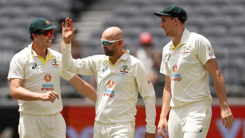 Pat Cummins and Cameron Green congratulate Australia bowler Nathan Lyon on a wicket in a Test against West Indies.