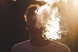 Boy with an E-cigarette or vaping, blowing smoke into the sky