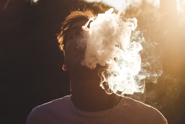 Boy with an E-cigarette or vaping, blowing smoke into the sky
