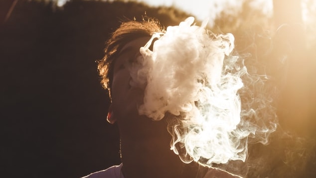 Boy with an E-cigarette or vaping, blowing smoke into the sky