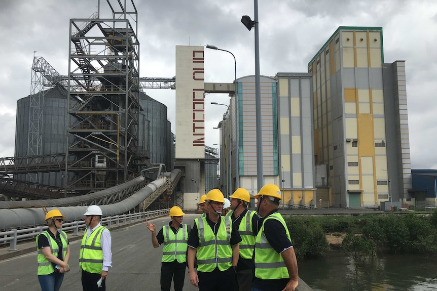 A group of people in front of a large flour milling facility.